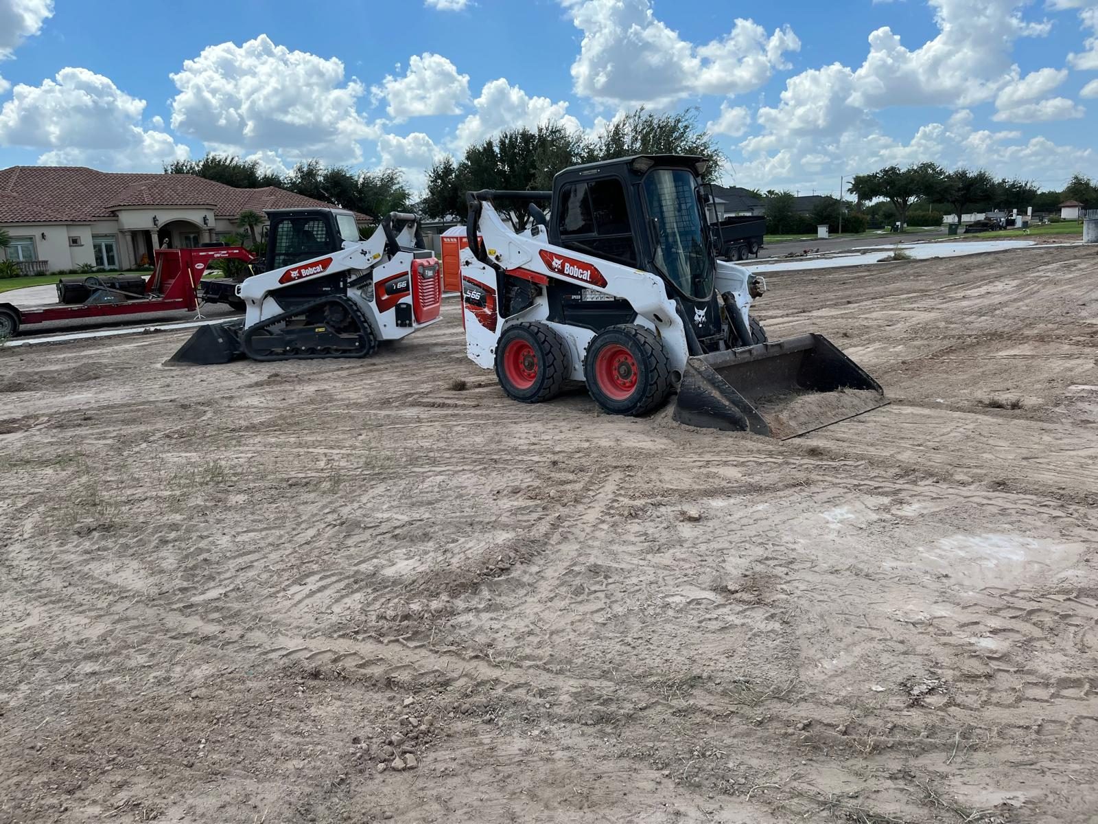 Two skid steers working on a dirt pad